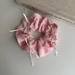 Detailed view of pink knitted scrunchie featuring elegant white ribbon bow accents