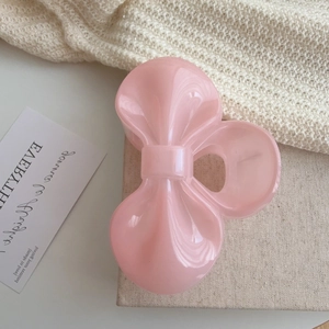 Pink resin bow hair clip in a French style aesthetic on a soft fabric background