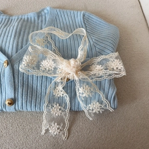 Detail of floral lace bow hair tie over blue knit cardigan with gold buttons