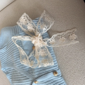 Close-up of light blue knit top featuring ribbed texture, lace bow, and gold buttons
