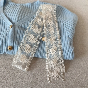 Detail of light blue knit cardigan with gold buttons and floral lace ribbon accessory