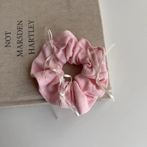 Close-up of pink knit scrunchie with white bows on a book, high-quality hair accessory
