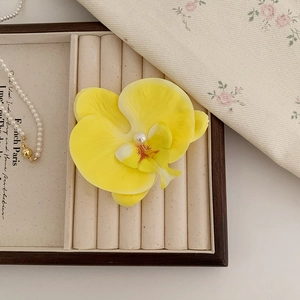 Détail de la pince à cheveux orchidée jaune avec perle sur un plateau à bijoux