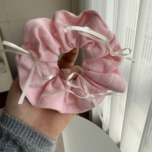 Detail of pink knitted scrunchie with lace texture and small white ribbon bows