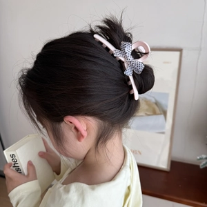 Détail d'une pince à cheveux rose avec un nœud à pois noirs et blancs sur une coiffure