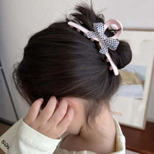 Détail d'une pince à cheveux rose avec un nœud gris à pois sur une coiffure d'enfant