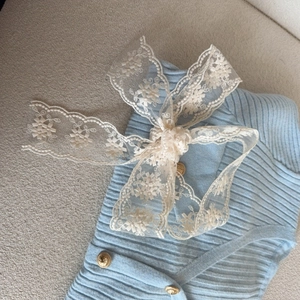 Elegant light blue ribbed knit cardigan featuring large beige lace bow and vintage gold buttons