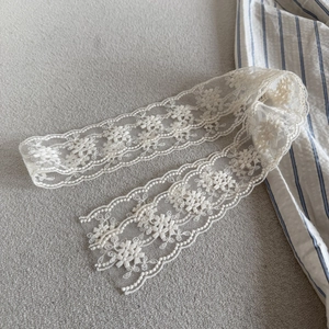 Beige floral lace hair ribbon with embroidery and scalloped edges on a textured background