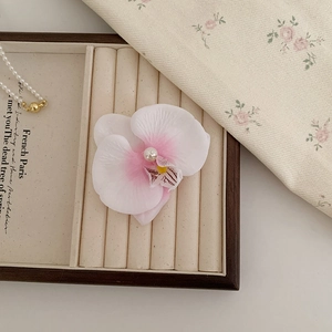 Détail macro d'une pince à cheveux orchidée avec pétales dégradés et perle centrale
