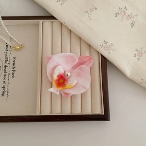 Détail de la pince orchidée avec pétales dégradés roses et une perle blanche au centre