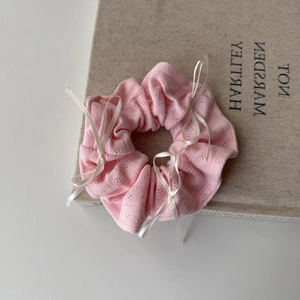 Pink knit scrunchie with white ribbon bows displayed on a book for hair styling