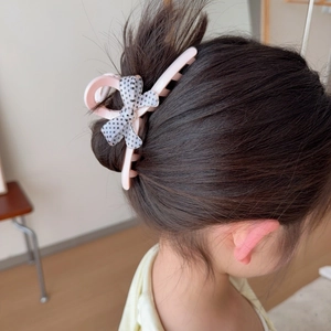 Pince à cheveux rose avec nœud à pois sur un chignon d'enfant, vue arrière