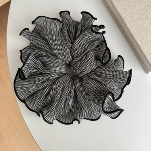 Détail d'un chouchou à motif pied-de-poule et bords volantés sur une table blanche
