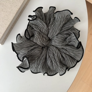 Chouchou élégant à motif pied-de-poule avec bords à volants sur une table blanche