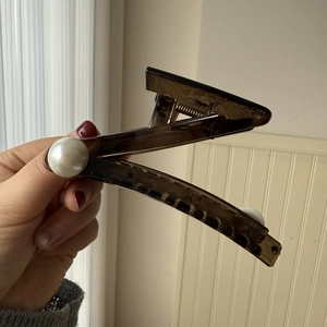 Detail showing deep brown resin hair claw clip with large pearl accents and metal spring