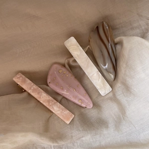 Close-up of elegant acetate hair clips set with marble patterns and gold foil on beige cloth