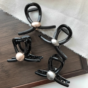 Dettaglio di fermagli neri con perle metalliche su legno scuro e tessuto di lino