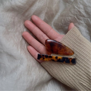 Detailed view of tortoiseshell pattern acetate hair clips held by hand for size reference