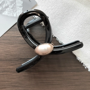 Pinza per capelli nera minimalista con dettaglio metallico oro champagne su legno scuro