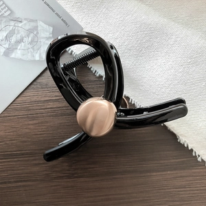 Dettaglio molletta per capelli nera con inserto in metallo oro rosa su piano legno