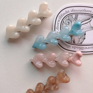Detail of four heart-shaped resin hair clips in pastel colors and marble textures