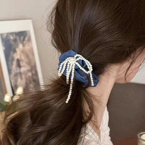 Chouchou en satin bleu avec nœud perlé porté au poignet dans un décor chaleureux