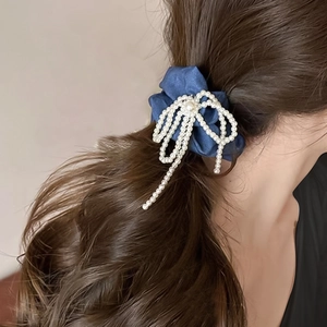 Gros plan d'un chouchou en satin bleu marine avec un nœud en perles blanches et pompons