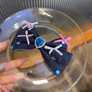 Detailed close-up of blue denim bow hair clip with heart rhinestone and ribbon accents