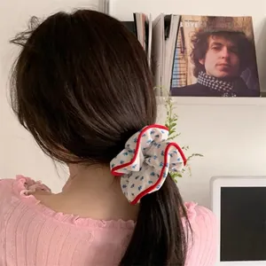 Détail d'un chouchou à fleurs bleues avec bord rouge sur une queue de cheval brune