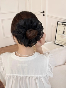 Dettaglio di un grande elastico scrunchie nero in organza trasparente su uno chignon elegante