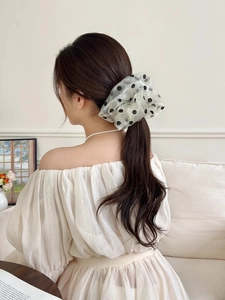 Dettaglio di un elastico in organza bianca a pois neri indossato su una coda alta