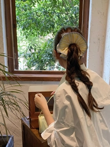 Close-up of oversized yellow striped scrunchie worn on a model's ponytail by a window