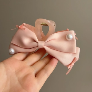 Dettaglio molletta per capelli con fiocco in raso rosa, perle e nastrini decorativi