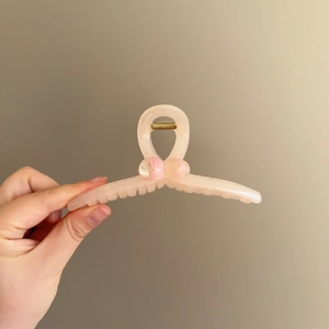 Detail of peach pink wheat-shaped hair claw clip with golden metal spring and smooth texture