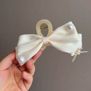 Dettaglio della pinza per capelli in raso crema con eleganti perle e piccolo fiocco nastro
