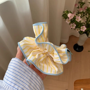 Detail of yellow and white striped oversized scrunchie with blue edging held by a model