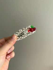 Détail d'une barrette à cheveux en perles cerises avec fruits rouges et feuilles vertes