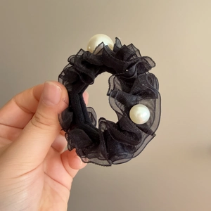 Détail d'un chouchou en organza noir avec de grandes perles et une texture plissée chic