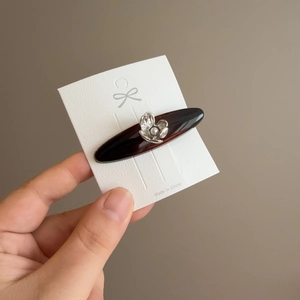 Detail of tortoise shell hair clip with silver metal flower and pearl on card