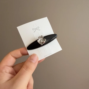 Elegant black acetate hair clip with silver flower and pearl detail on display card