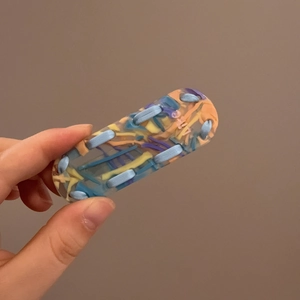 Detail of checkered resin hair clip with woven blue yellow and orange ribbons