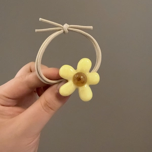 Gros plan d'un chouchou fleur jaune avec perle ambrée tenu à la main sur un fond gris neutre