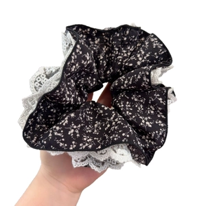 Main tenant un chouchou floral noir avec bordure en dentelle blanche de style vintage