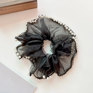 Détail d'un chouchou en maille noire orné de perles blanches élégantes sur les bords