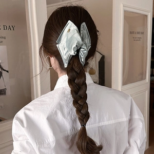 Détail de la pince à cheveux noeud en satin vert clair avec étiquette dorée sur tresse