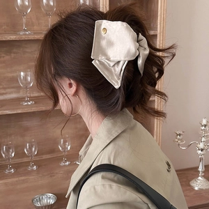 Vue détaillée d'une pince à cheveux en satin champagne avec emblème doré sur soie douce