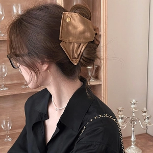 Détail d'une pince à cheveux nœud en satin marron avec logo doré sur un chignon