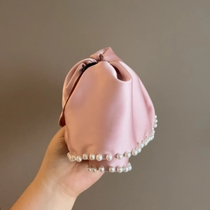 Pink satin drawstring hair accessory with pearl trim shown held in hand