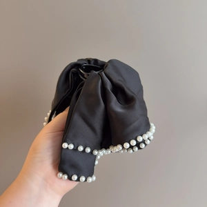 Detail of a large black satin bow hair claw clip with elegant white pearl trim