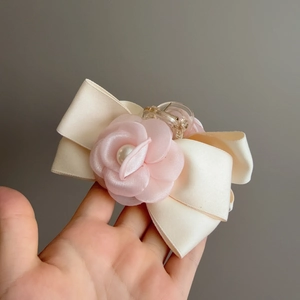 Détail de la pince à cheveux avec nœud crème, camélia en satin rose et perle